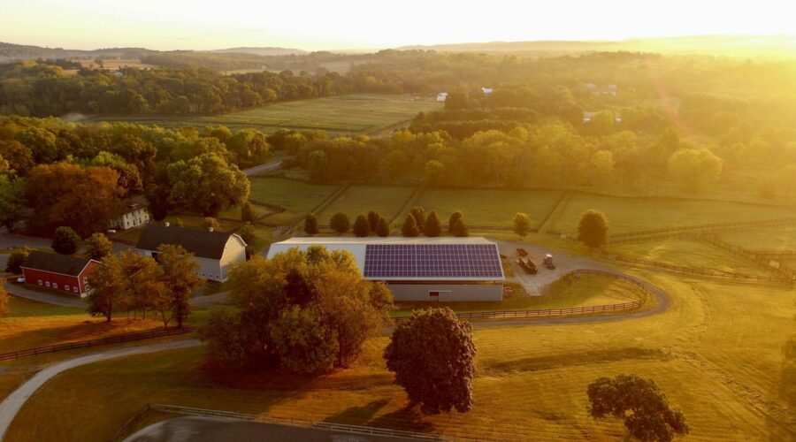 Sunset on a rural landscape that centers a barn with solar panels on the roof.
