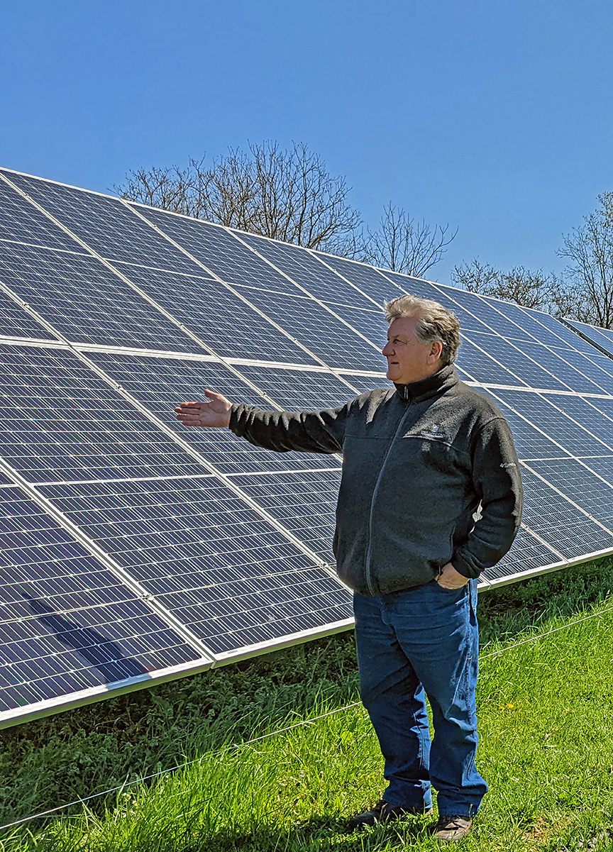 A farmer gestures towards a solar array in his field as he talks.