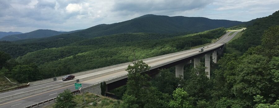 A massive divided four lane highway with a bridge over a valley with only mountains surrounding.