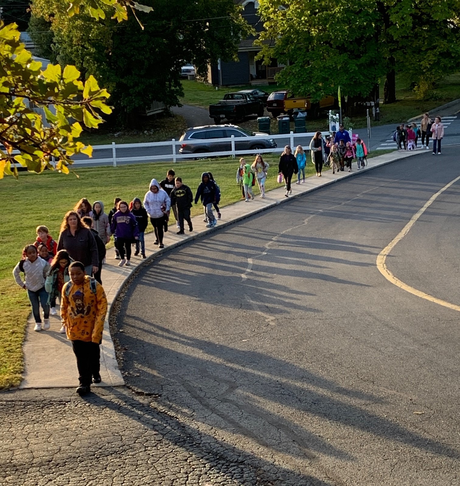 A line of children walk along a sidewalk together.