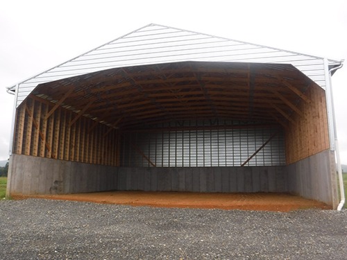 A large empty, three-sided structure with a roof and a floor and open front meant for animal waste storage.