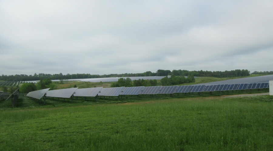 A solar array tucked away between green shrubs and fields under a cloudy sky.