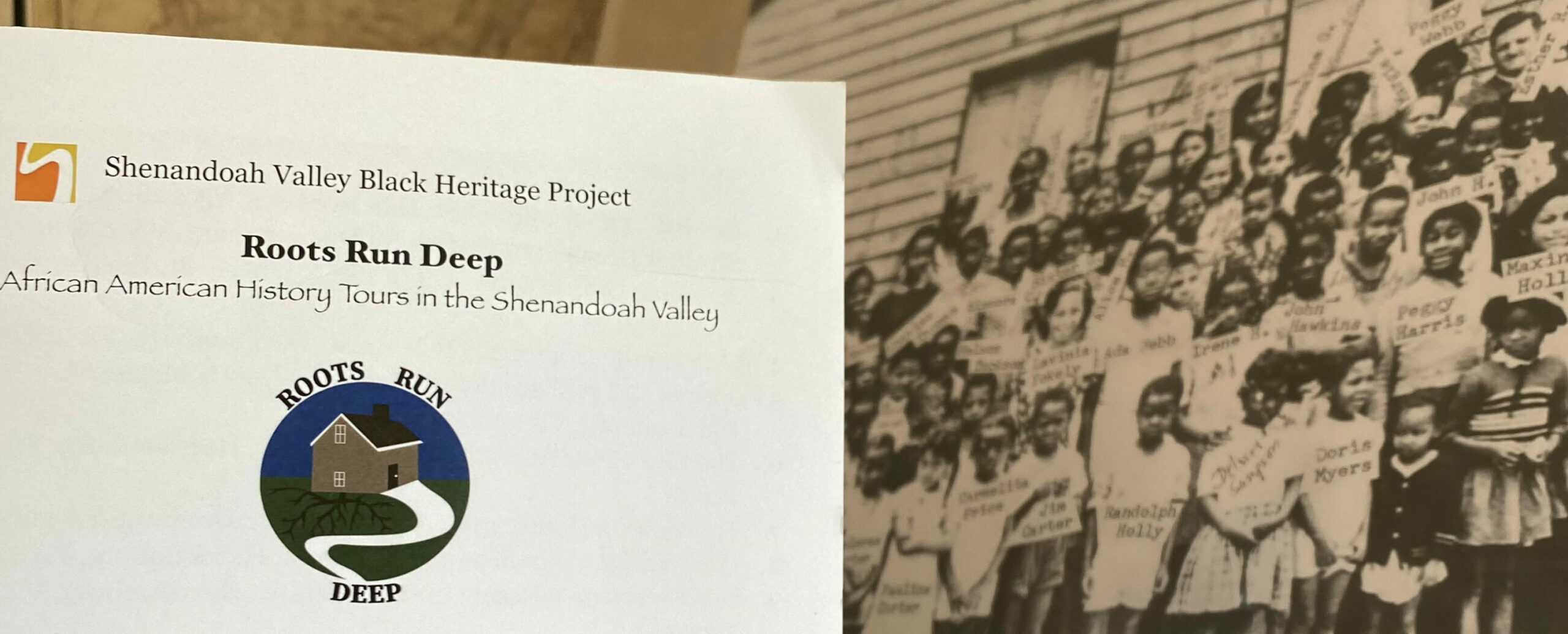 A brochure for the roots run deep tours in Harrisonburg, Virginia sits in front of an aged black and white photo of Black students gathered and posing for the photo outside of what appears to be a school building.