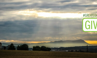 Sun shines through the clouds over the iconic Massanutten Mountain with farm fields in the foreground.