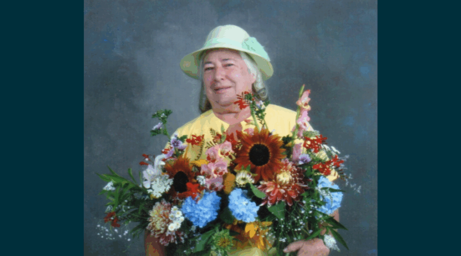 Juanita smiles while holding a large bouquet of her flowers, in front of a blue background