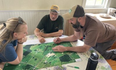 Three people lean in around an areal map.