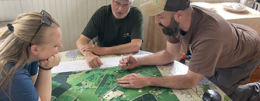 Three people lean in around an areal map.