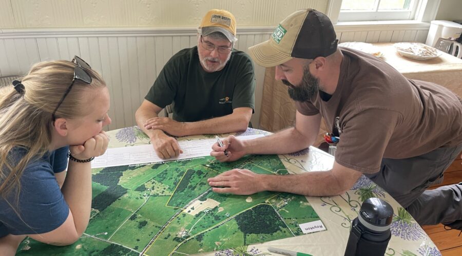 Three people lean in around an areal map.