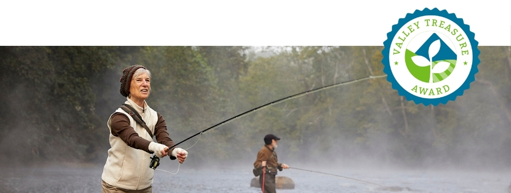 A Valley Treasure Award seal overlay a photo of a woman standing in what looks like a cold misty river casting a fly reel.
